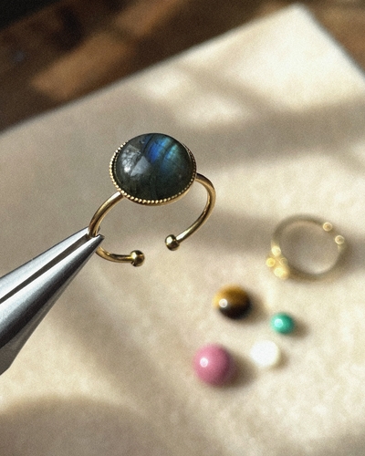 Photo d'une pince qui tient une bague support d'un cabochon d'une pierre bleue